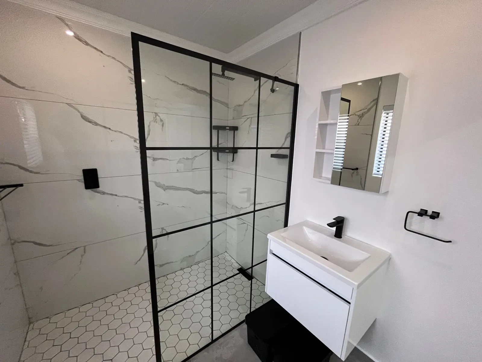 Black grid shower screen with marble-look tiles and wall-hung vanity